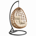 Sillón colgante de ratán sintético con cojines beige y estructura de acero negro